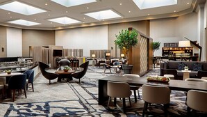 Un espacioso vestíbulo de hotel con una zona de estar central, un bar y un comedor.