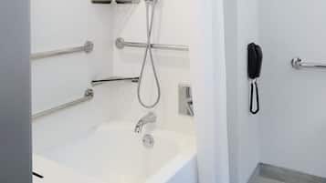 Un baño moderno con una bañera blanca, barras de apoyo, cabezal de ducha de mano y un teléfono montado en la pared.