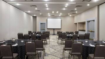 A conference room with multiple tables and chairs, a projector screen, and a carpeted floor.