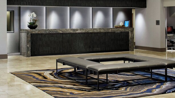 Un moderno vestíbulo de hotel con una recepción, una lámpara colgante grande y una alfombra con diseño.