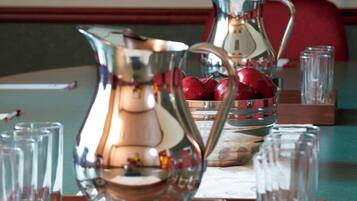 A table with a pitcher, a glass pitcher, and a bowl of apples. There are also several glasses and a power strip on the table.
