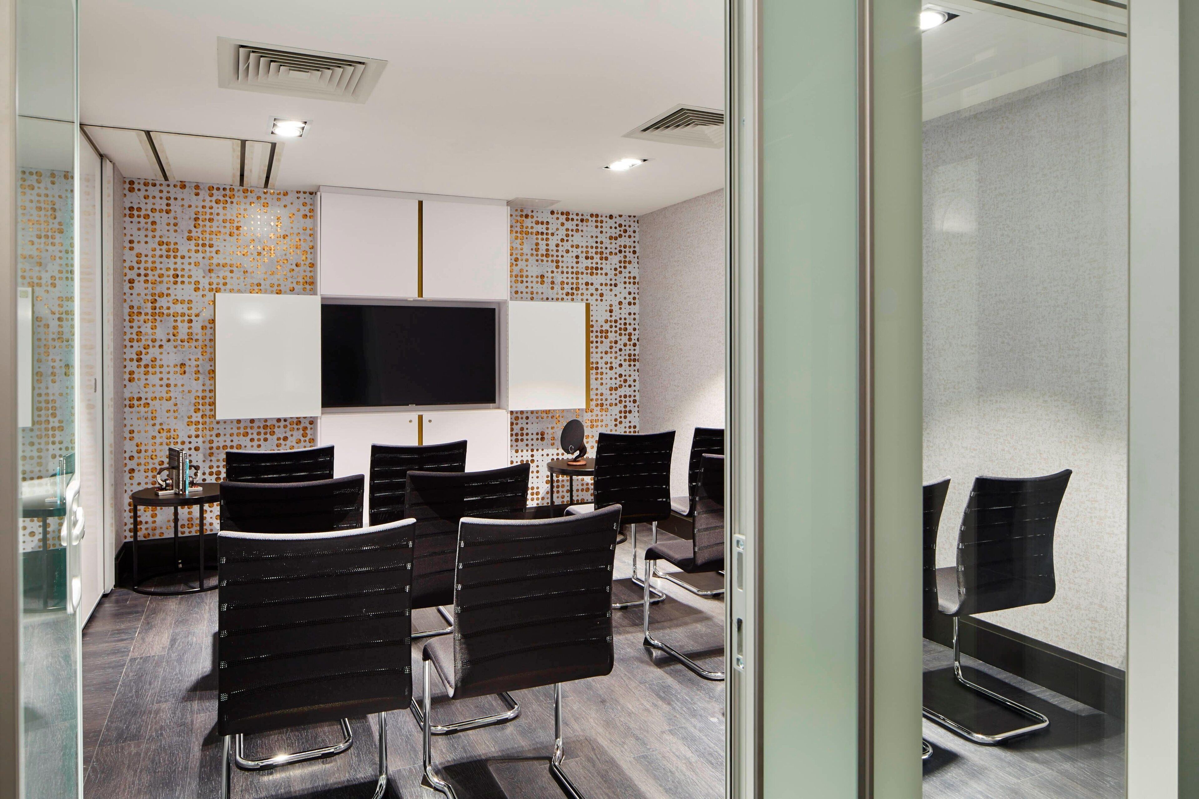 A modern waiting area with a flat-screen TV, black chairs, and a patterned wall.