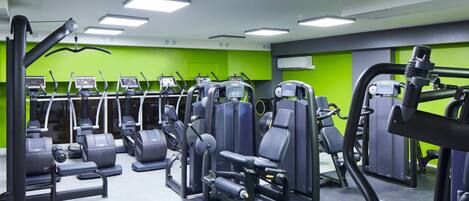 Un gimnasio con diversas máquinas de ejercicio, iluminación brillante y paredes verdes.