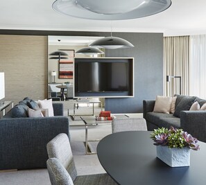 A modern living room with a large flat-screen TV, grey sofas, a coffee table, and a potted plant. - London Marriott Hotel Maida Vale (London)