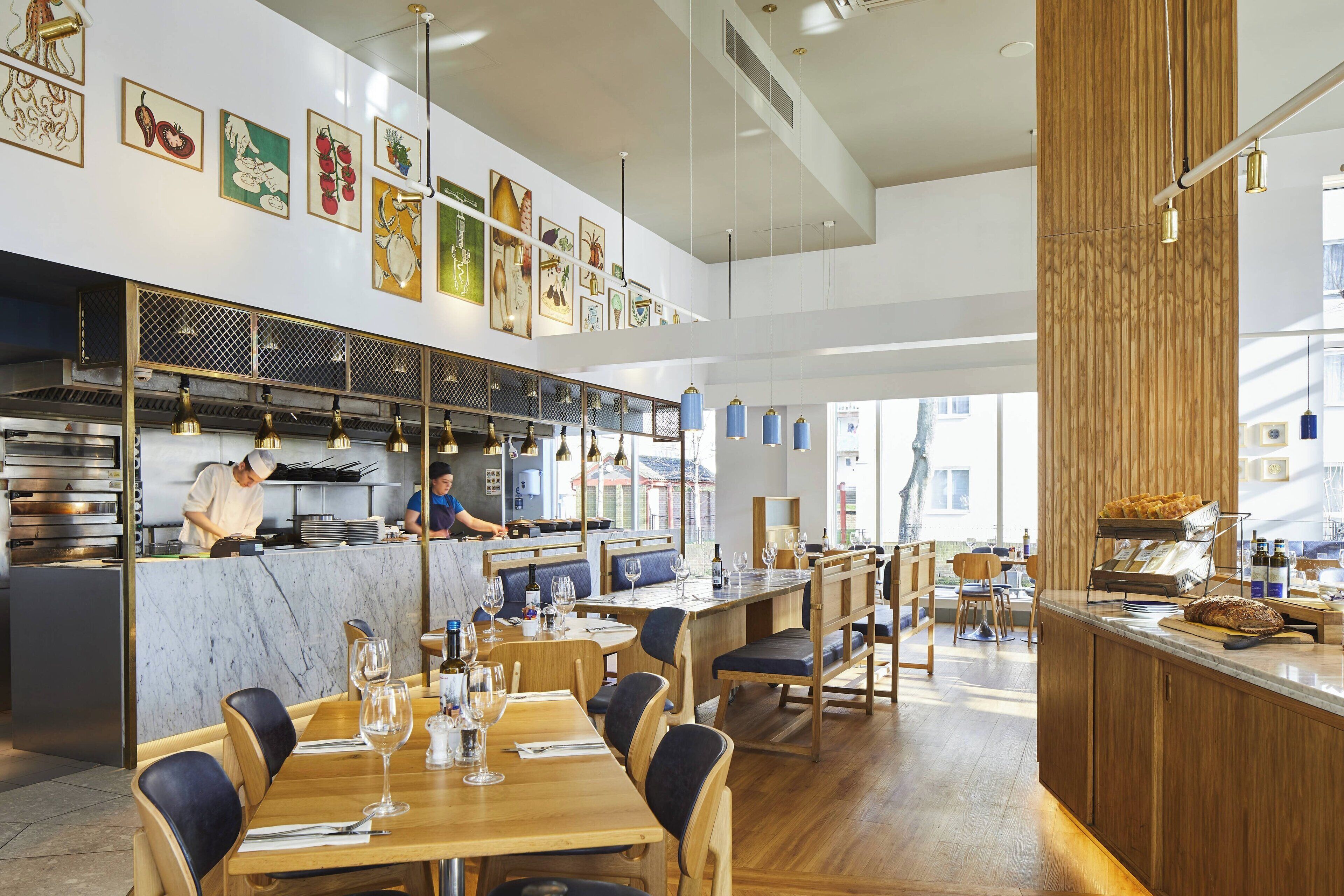 Un interno ristorante moderno con tavoli in legno, sedie blu e una zona cucina visibile sullo sfondo.