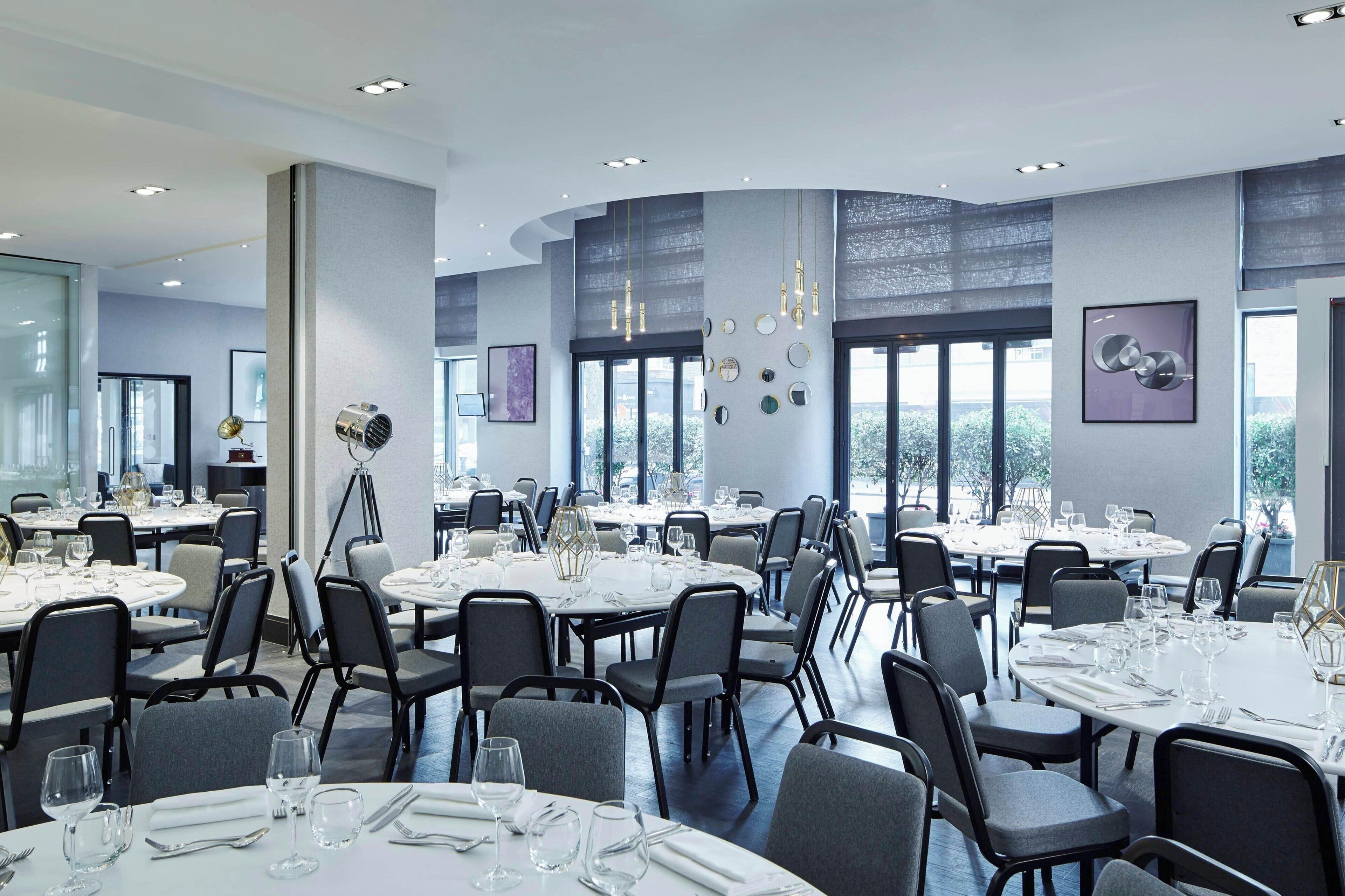 A modern dining area with round tables and chairs, large windows, and contemporary lighting fixtures.