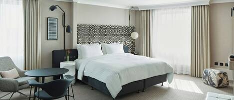 A modern hotel room with a large bed, a small table, a chair, and a sofa.