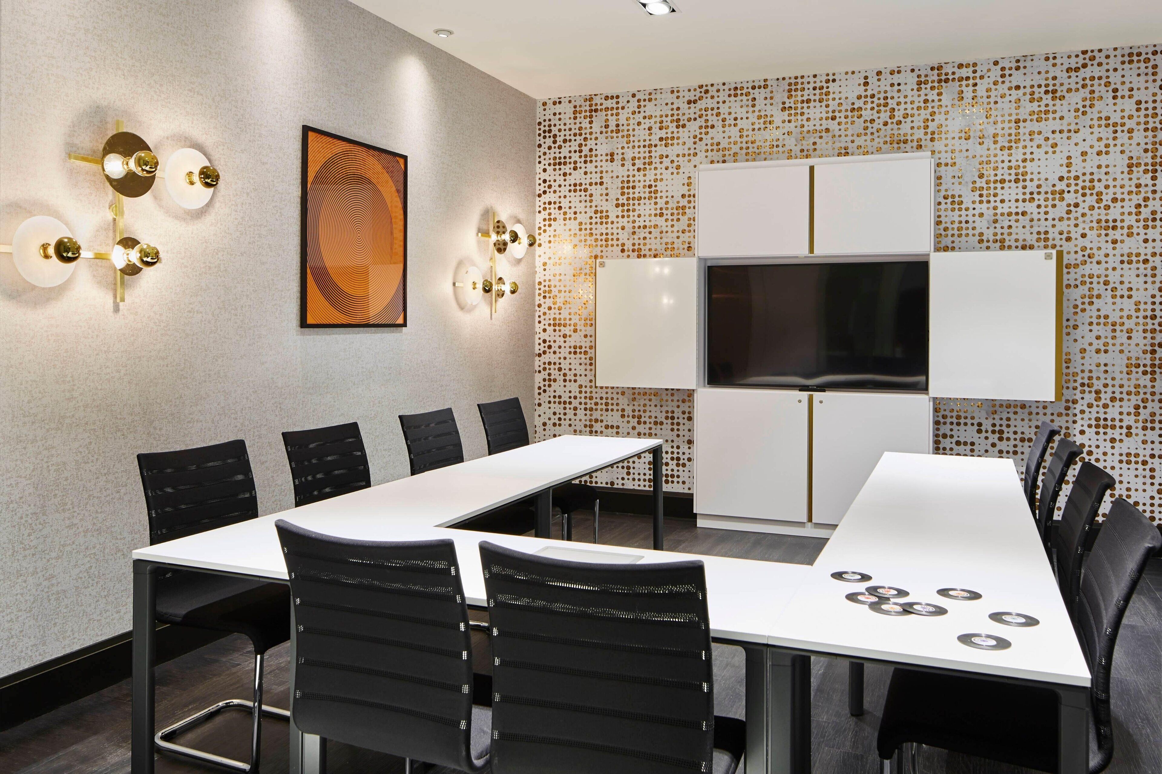 A modern conference room with a long table, black chairs, a white cabinet, and a mounted TV.