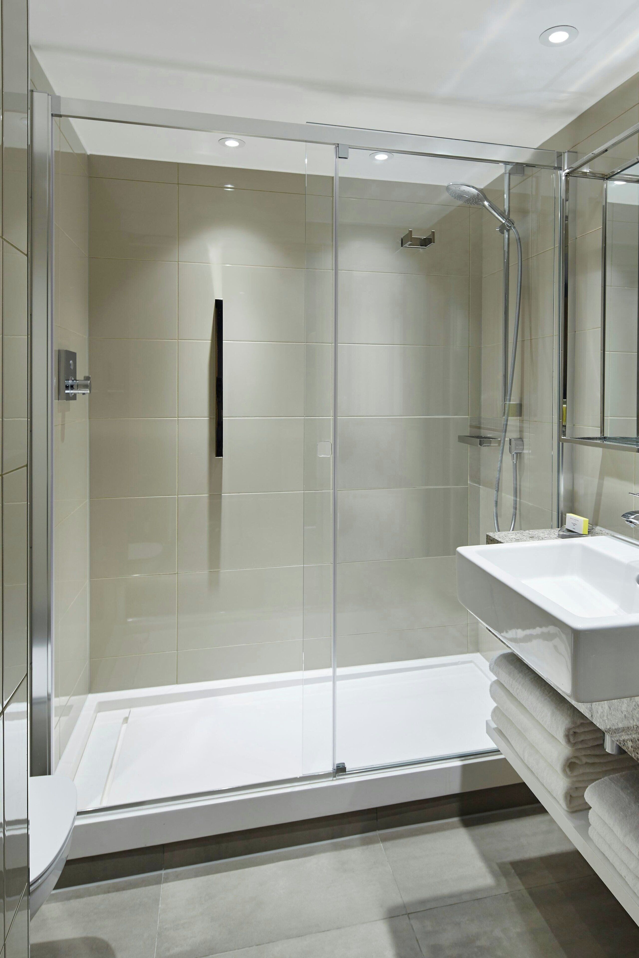 Un bany modern amb dutxa tancada amb vidre, un lavabo blanc i un mirall gran.