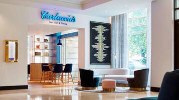 A modern hotel lobby with a bar, dining area, and seating.