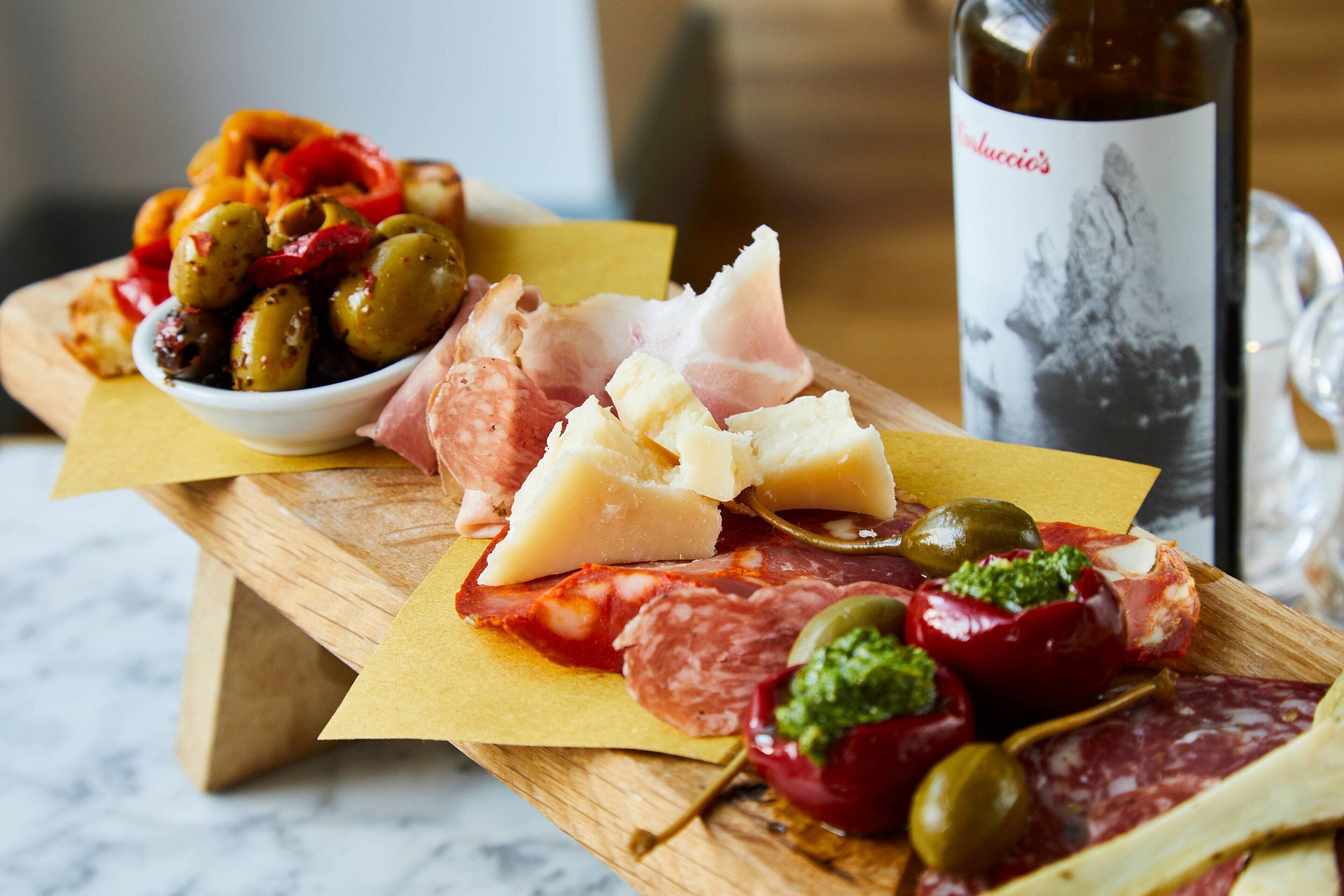 A wooden board with various cheeses, cured meats, and olives.