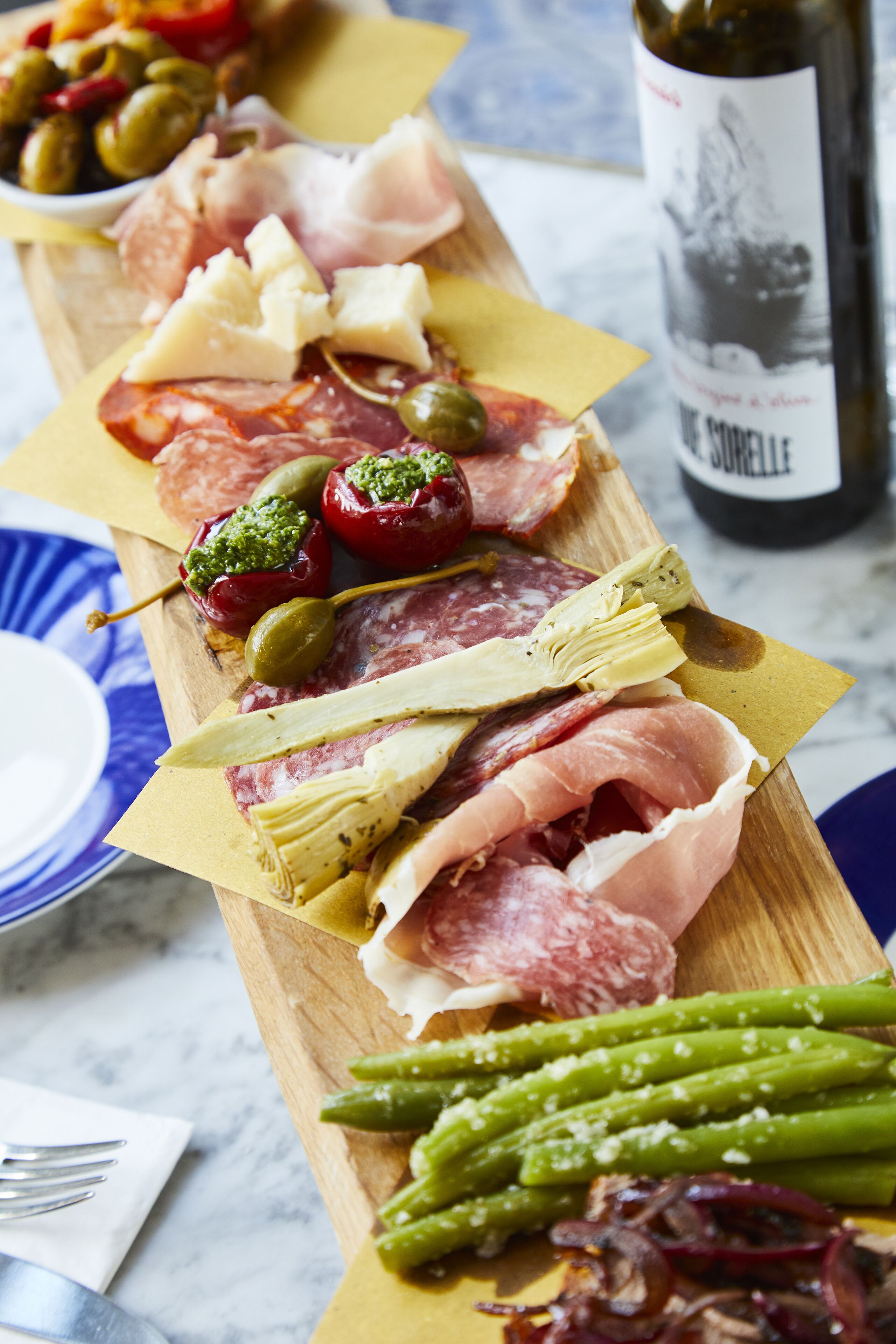 A charcuterie board with various meats, cheeses, olives, and asparagus on a wooden board.