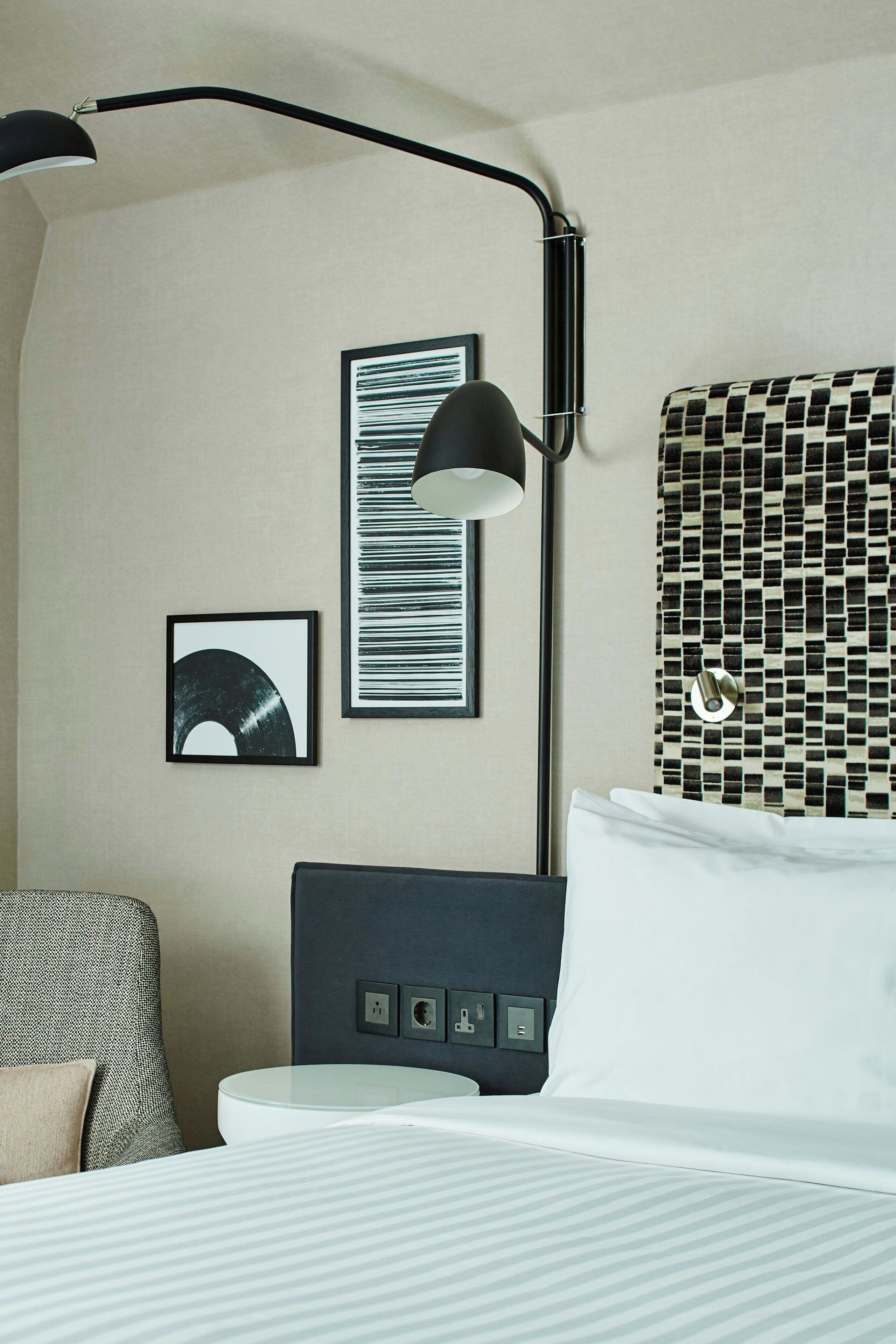 Una habitación de hotel con cama, escritorio, silla, lámpara y un cuadro en la pared.