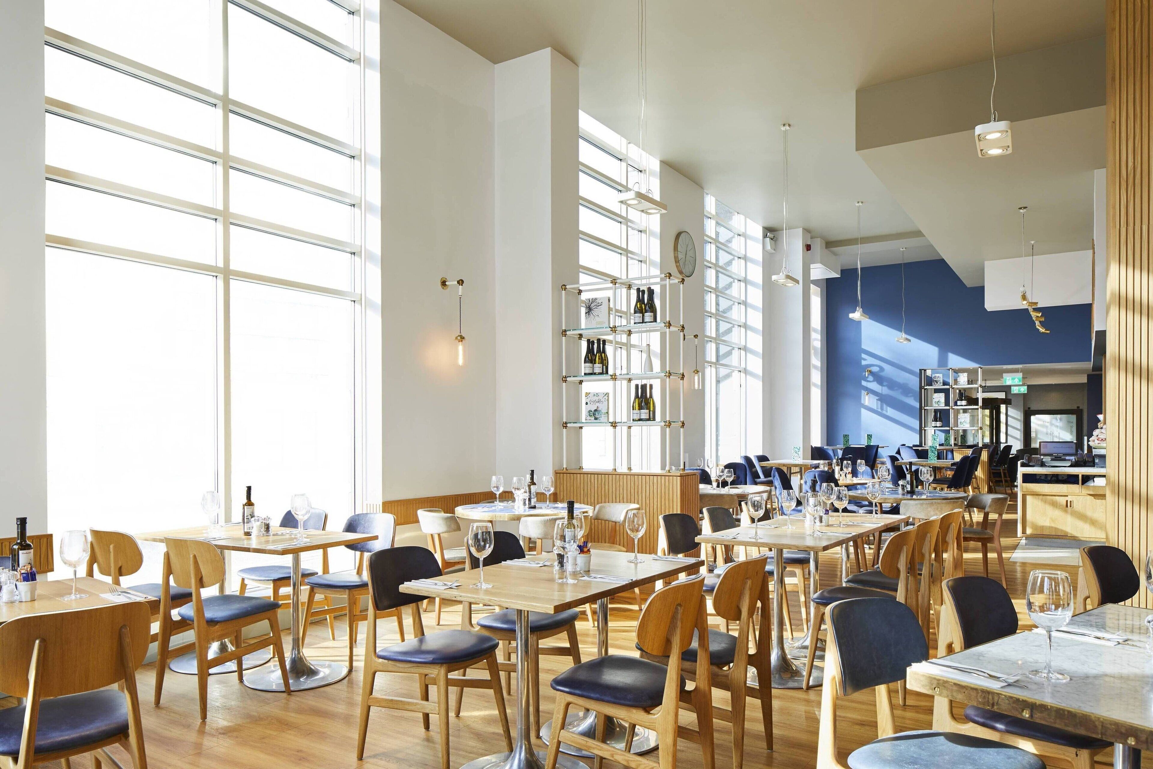 A spacious restaurant with high ceilings, large windows, and a variety of seating arrangements including tables and chairs.