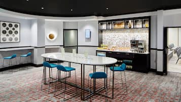 A modern conference room with a round table, blue chairs, a patterned carpet, and a kitchen area with a tiled backsplash.