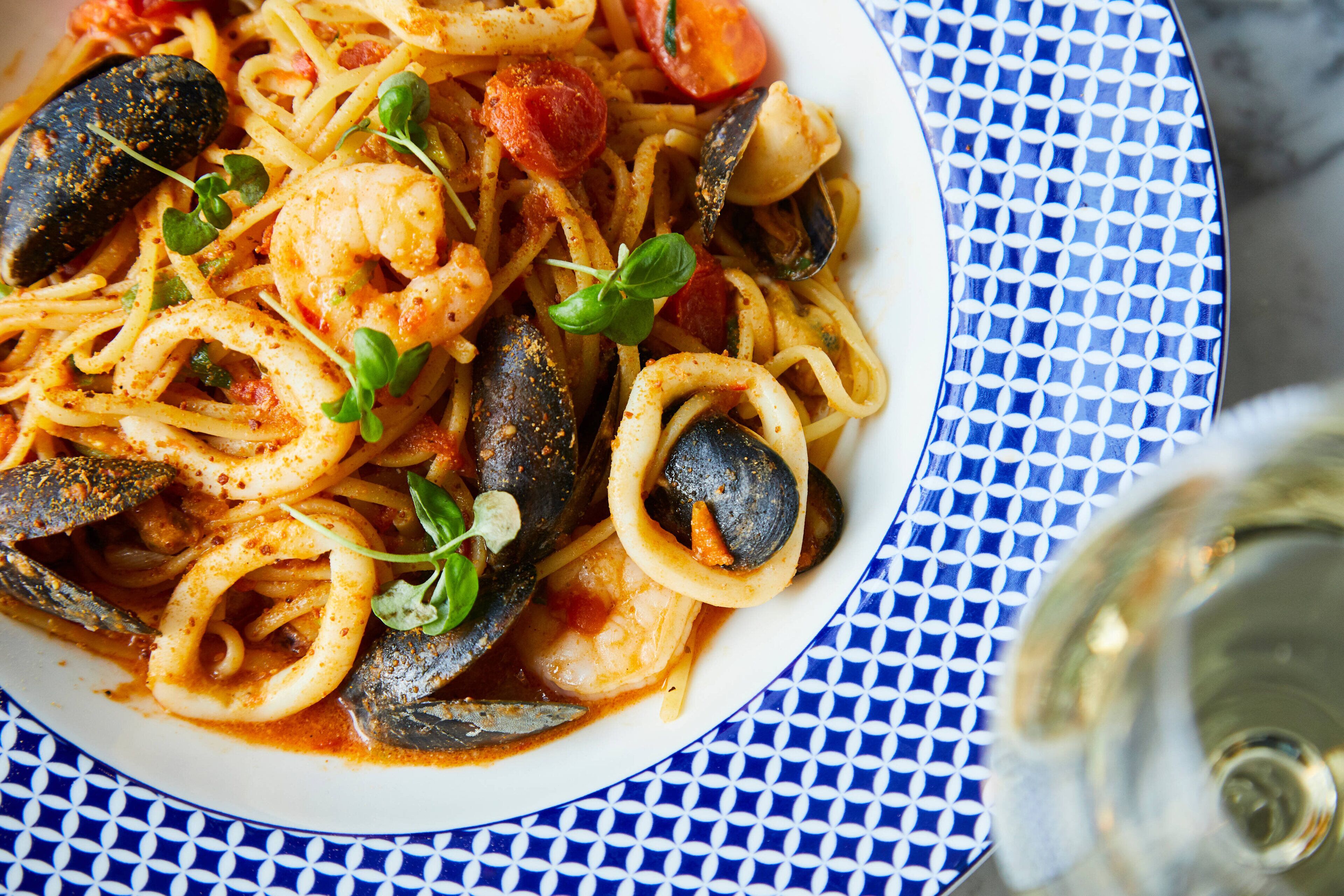 Een bord zeevruchtenpasta met mosselen, garnalen en inktvis, versierd met basilicum, op een bord met blauw-witte patronen.