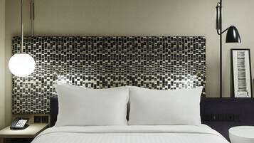 A hotel room with a bed, a nightstand with a phone, a wall-mounted lamp, and a framed picture.