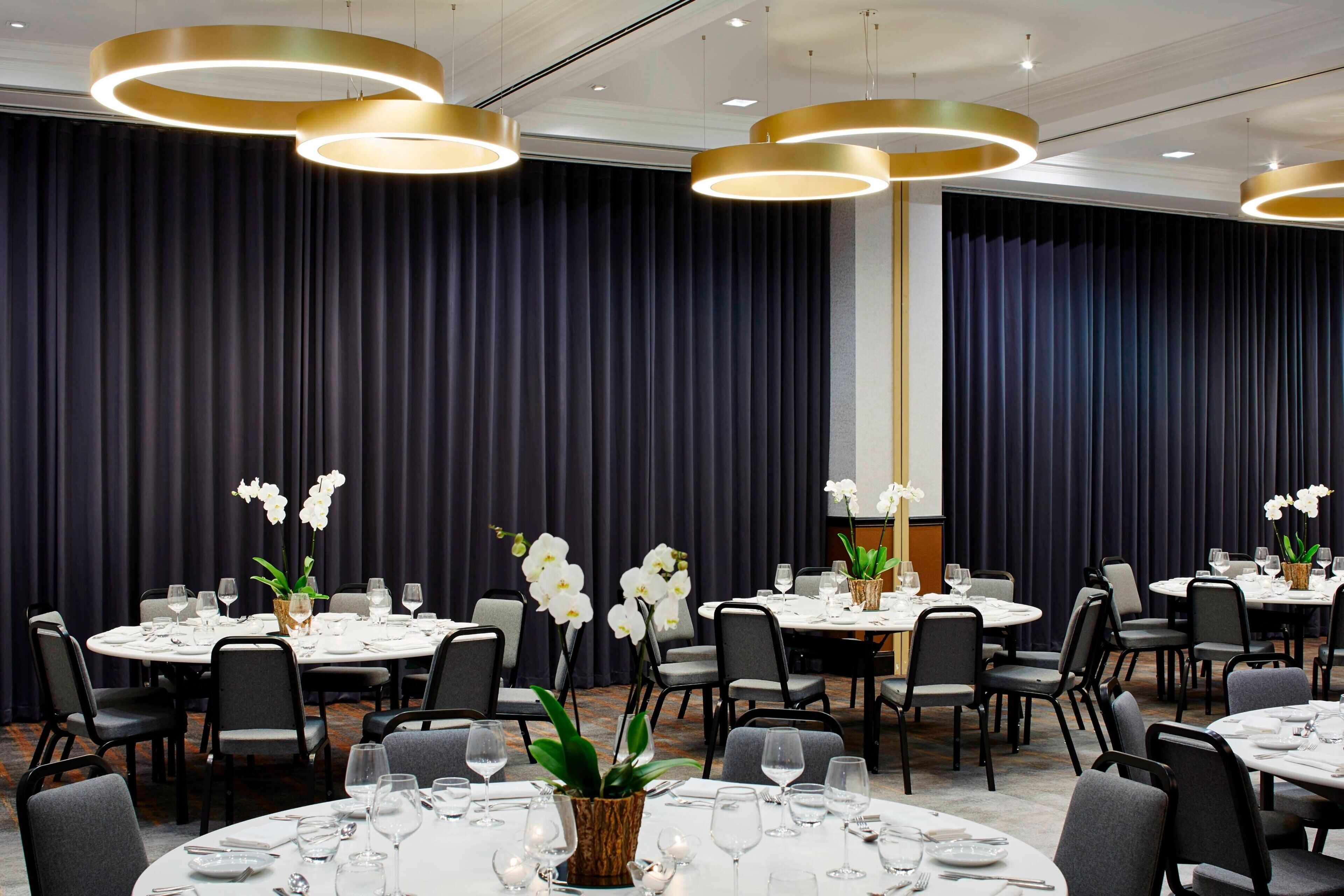A conference room with round tables, black chairs, and white table settings.