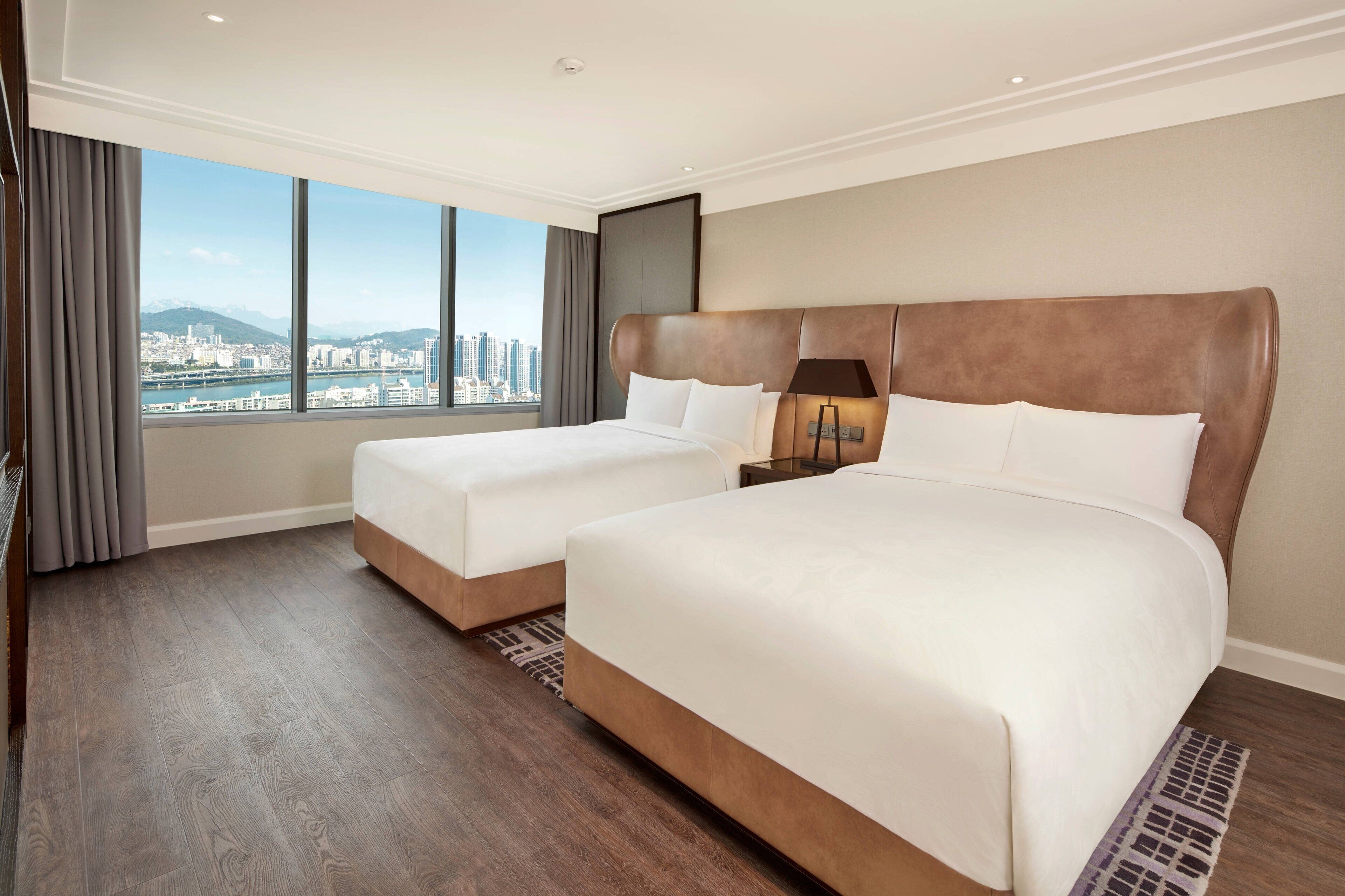 Ein Hotelzimmer mit zwei Betten, einem großen Fenster und Stadtblick sowie einem modernen Design.