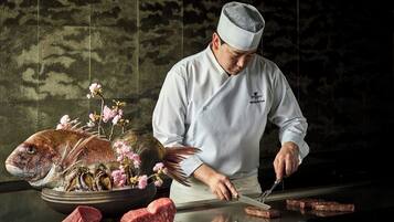 A chef preparing food at a counter with a fish, flowers, and meat.