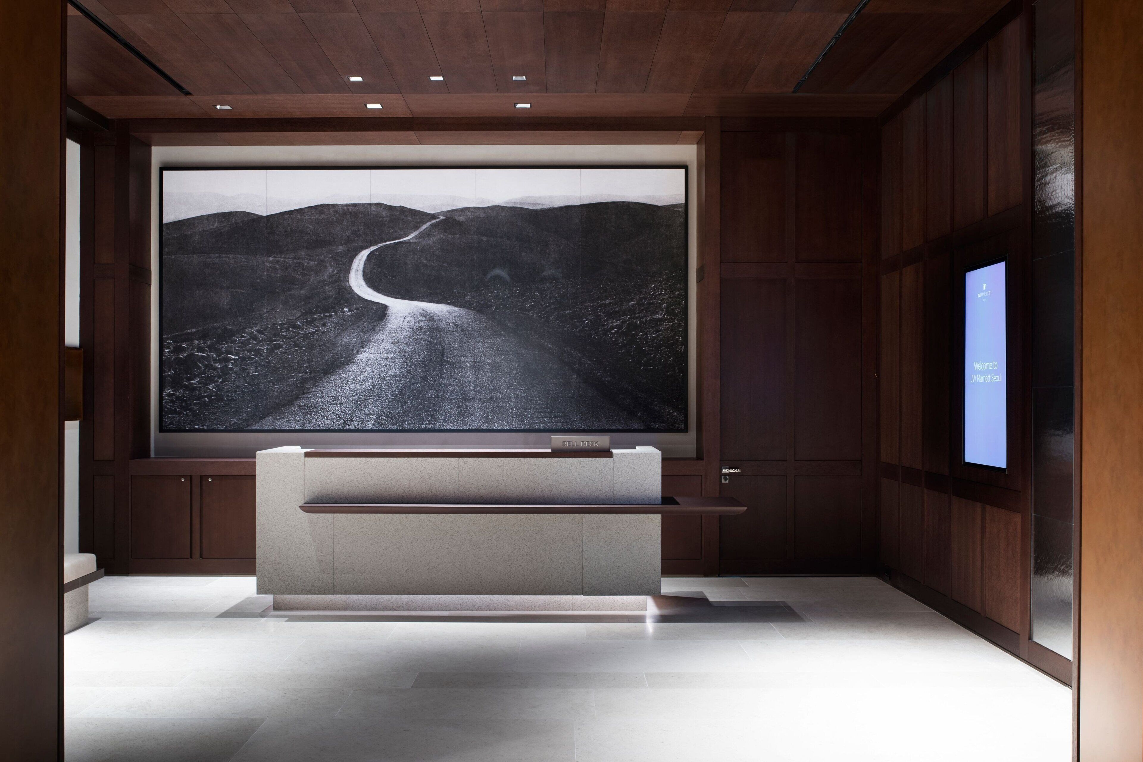 Een modern interieur met een groot scherm waarop een schilderachtige weg te zien is, houten lambrisering en een minimalistische bank.