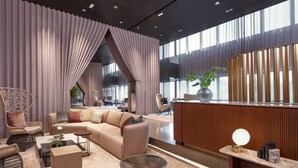 Un moderno vestíbulo de hotel con un sofá, sillas, un mostrador de recepción y ventanas amplias.