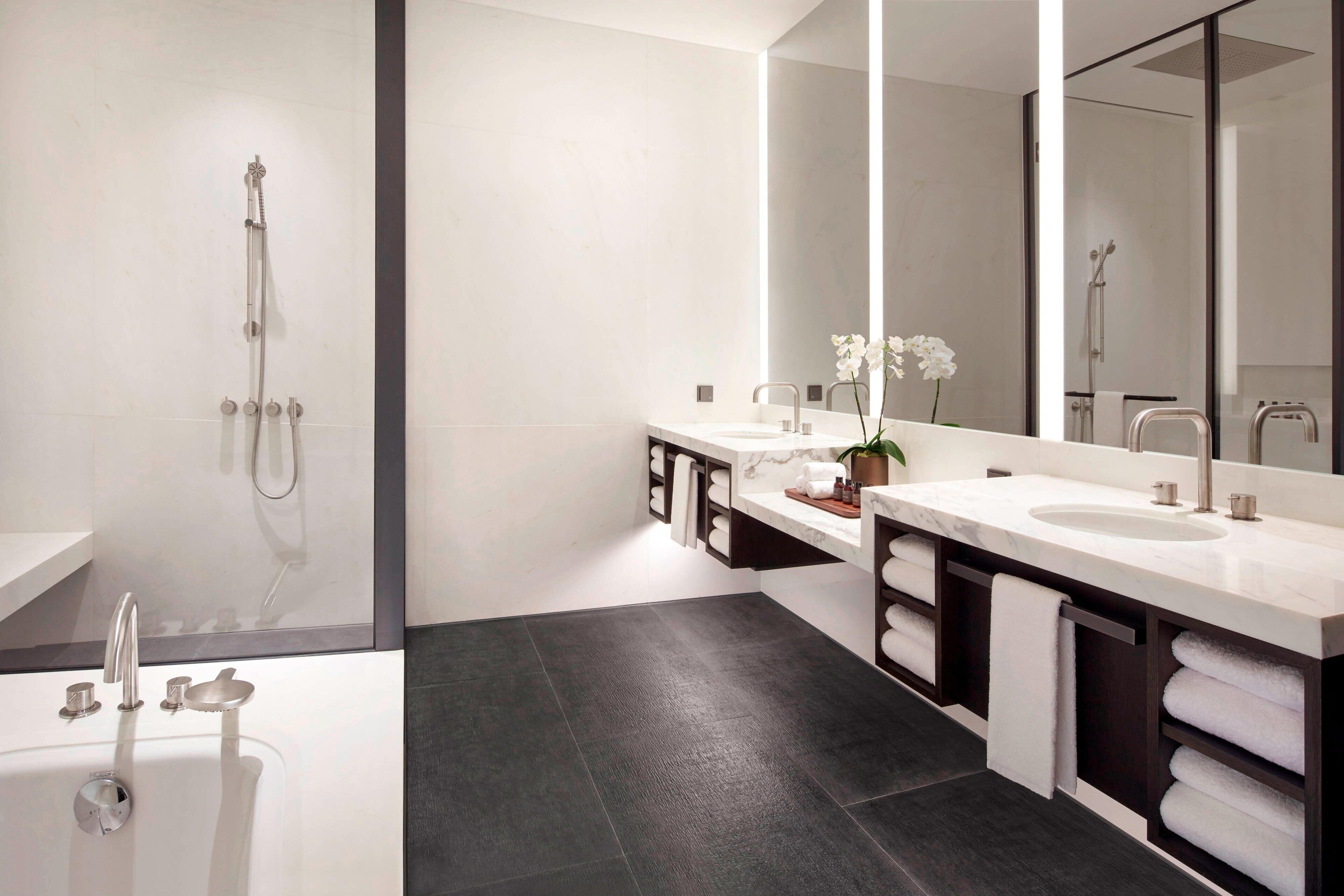 Une salle de bain moderne avec une baignoire, deux lavabos, un grand miroir et une douche.