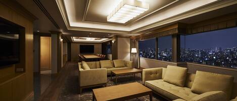 A spacious, elegantly furnished lounge with a city view, featuring sofas, a coffee table, and a television.