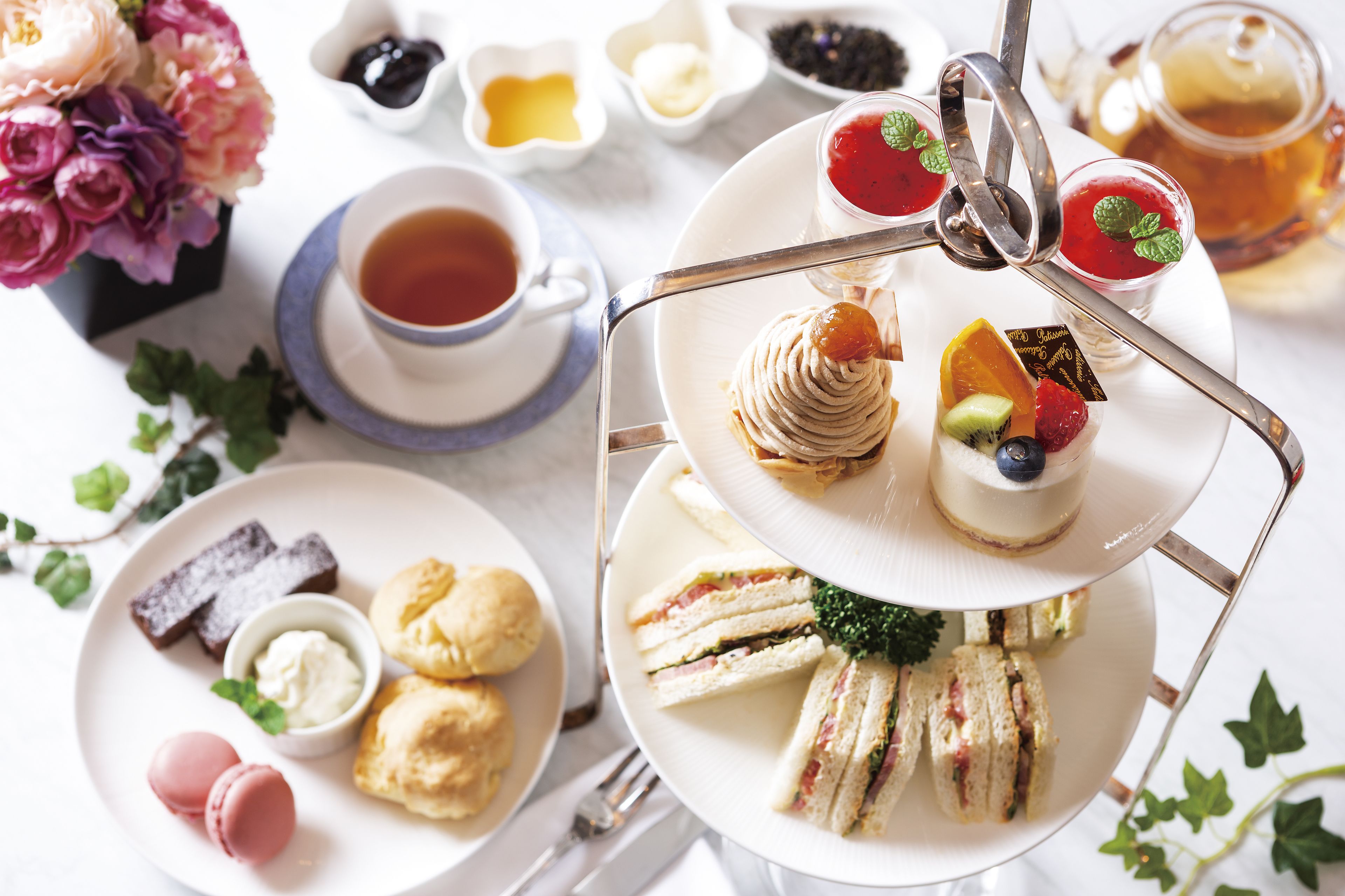 A multi-tiered dessert stand with various pastries and sandwiches, accompanied by cups of tea and small bowls of condiments.
