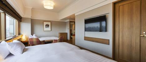 Habitación de hotel con una cama grande, un televisor montado en la pared, una puerta de madera y una ventana con cortinas.