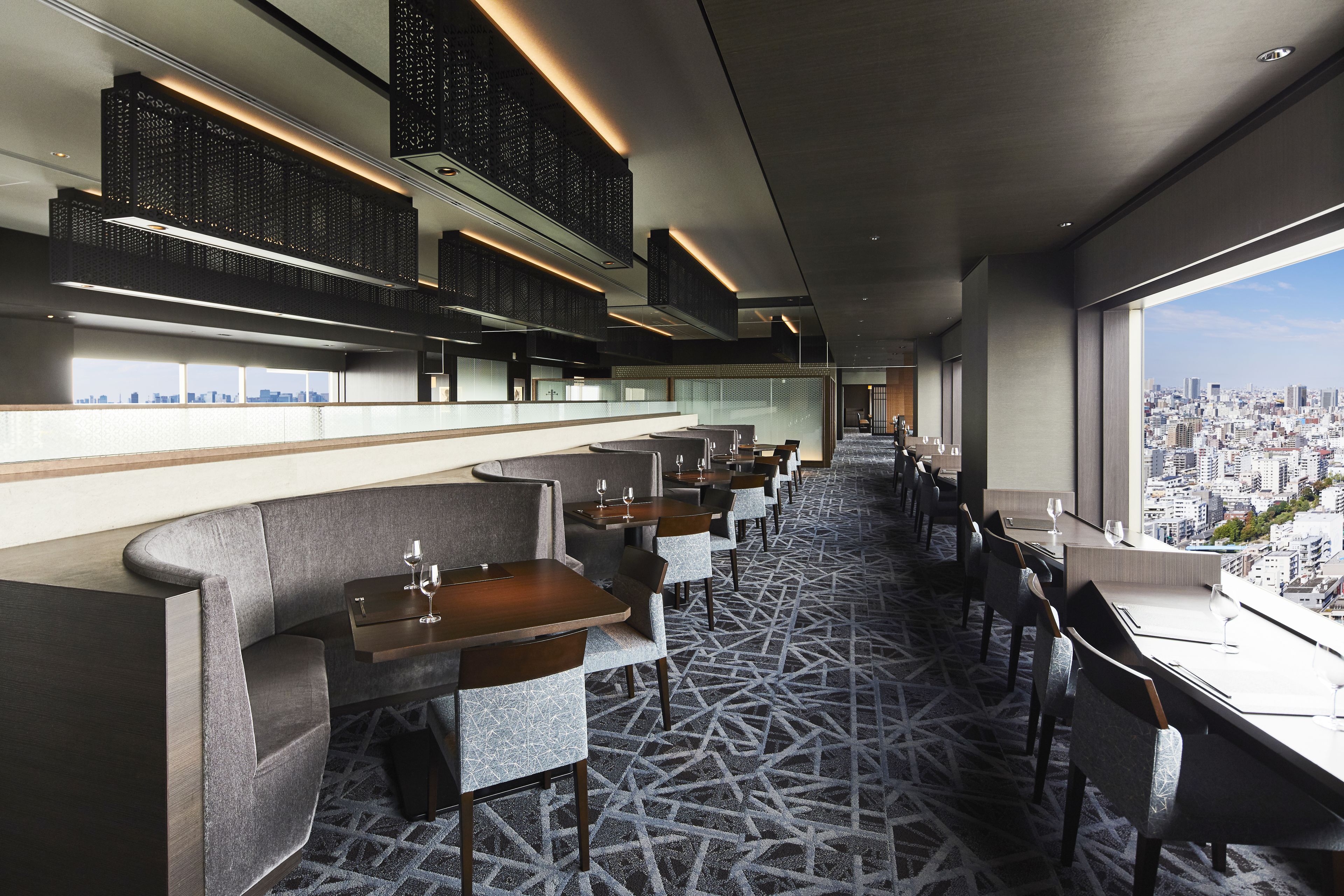A modern restaurant with a city view, featuring a long counter, cushioned seating, and patterned flooring.