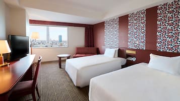 A hotel room with two beds, a desk with a TV, a chair, a small table, and a window with a city view.