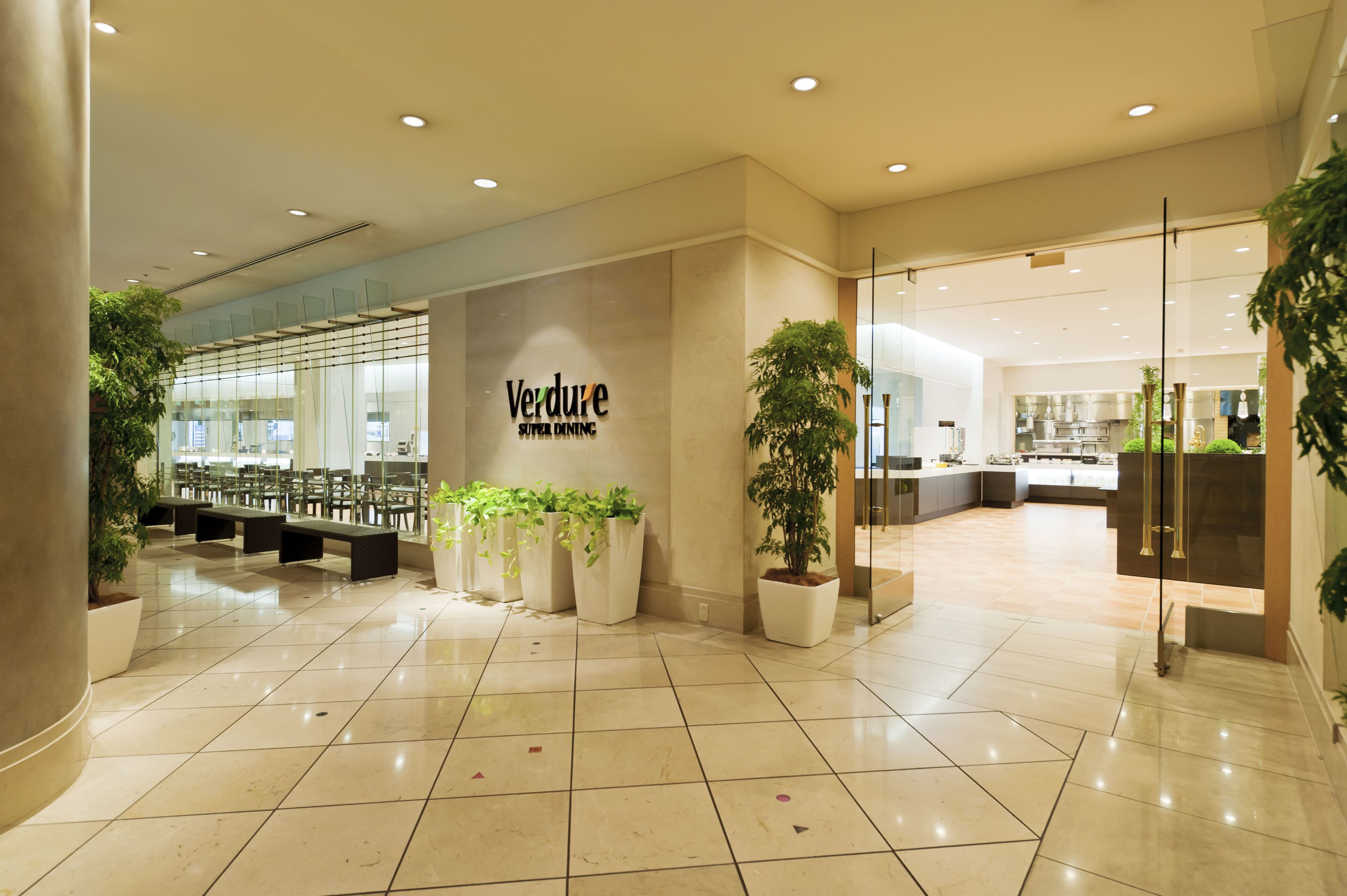 A modern interior with a 'Verdure Super Dining' sign, seating areas, and potted plants.