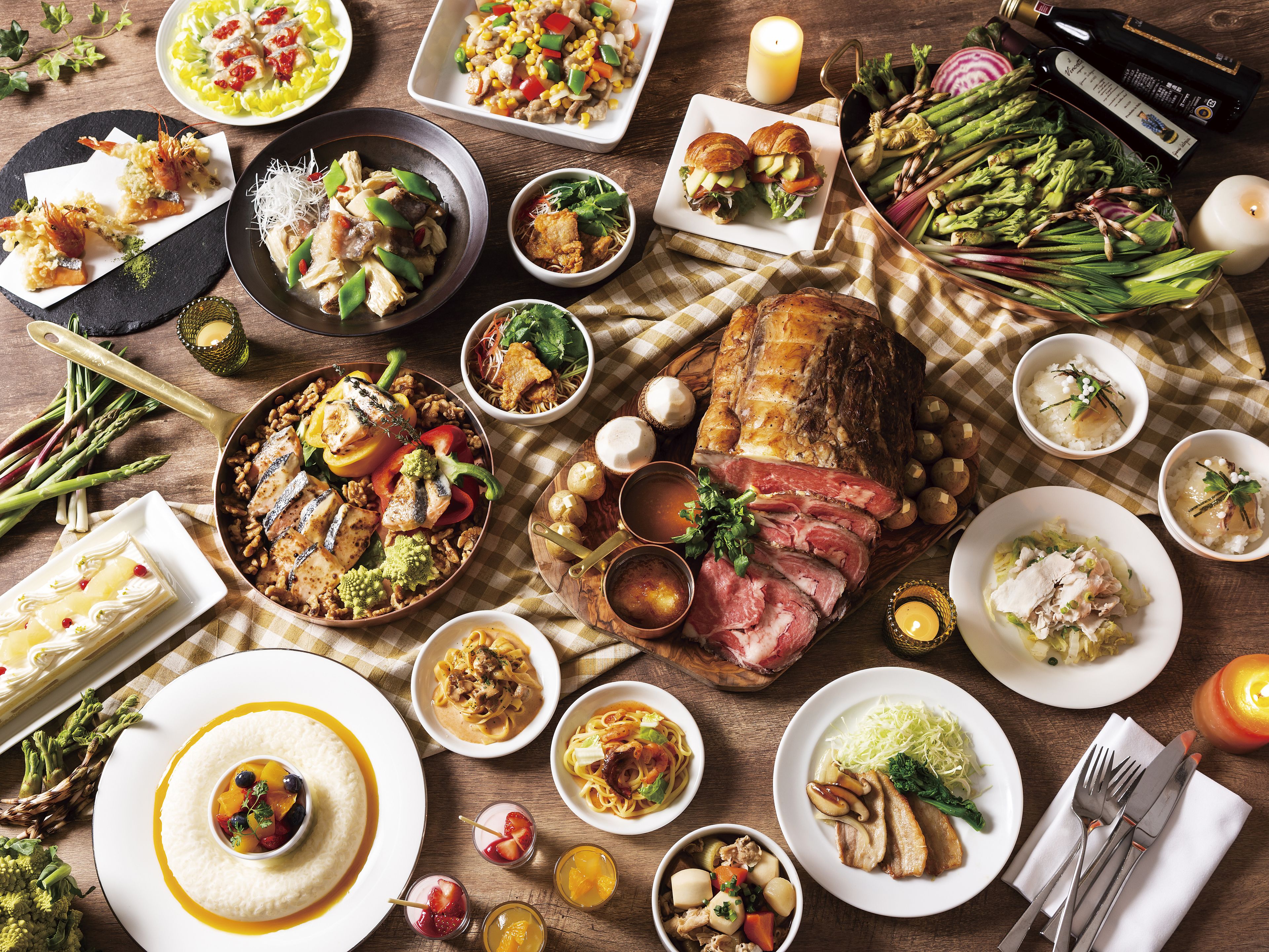 A variety of dishes including a roasted pork leg, pasta, and seafood, arranged on a wooden table.