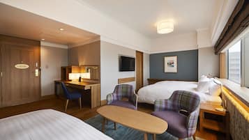 A hotel room with two beds, a desk, a chair, a small table, and a TV.