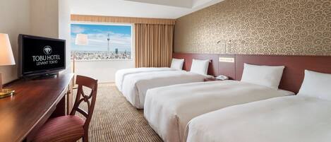 Habitación de hotel con dos camas, televisión, escritorio con lámpara y vista a la ciudad.