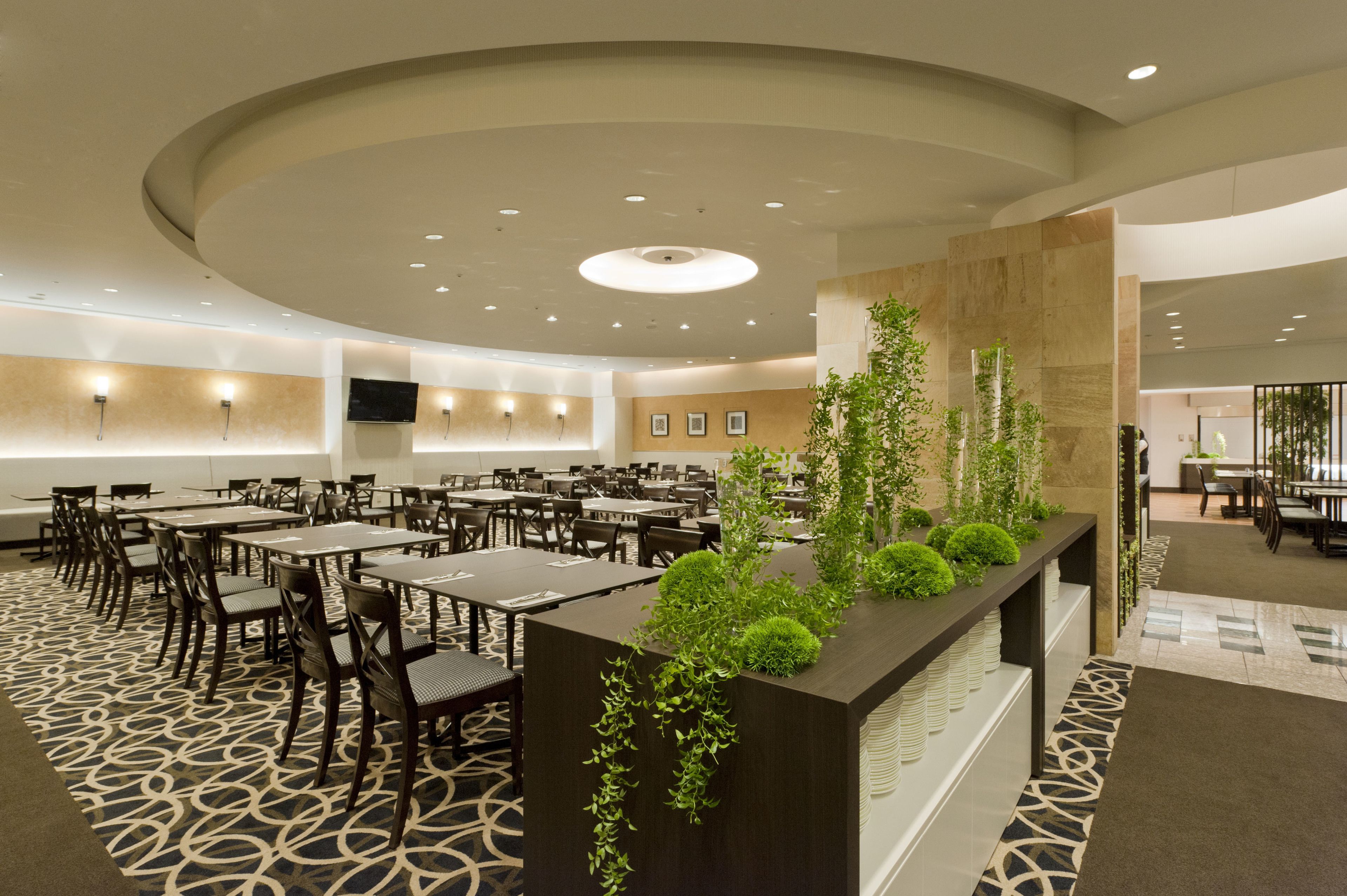 A spacious dining area with multiple tables and chairs, a central plant display, and a modern ceiling design.