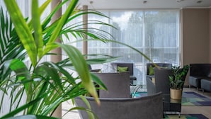 A modern hotel lobby with large windows, comfortable seating, and indoor plants. - Bellevue Park Hotel Riga (Riga)