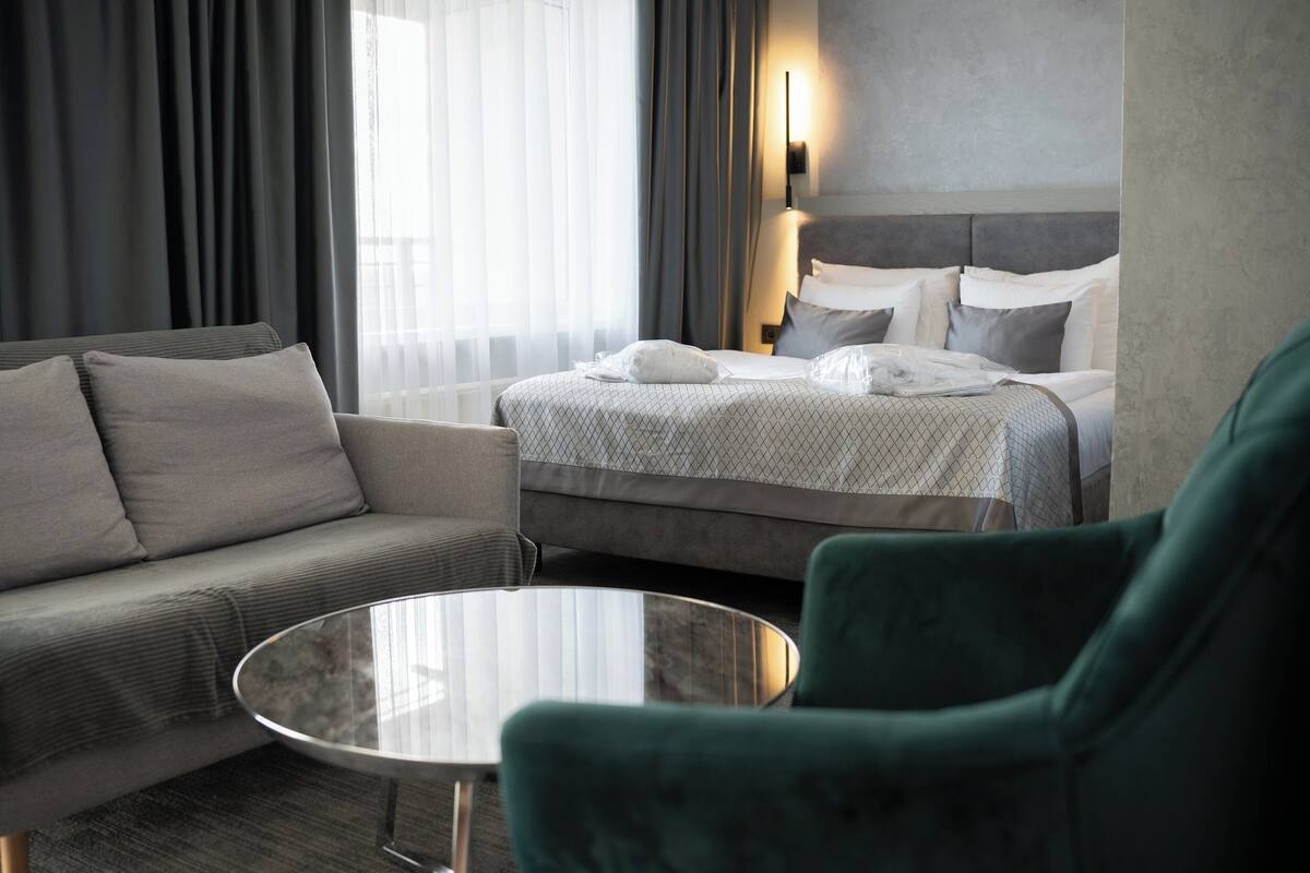 A hotel room with a bed, a sofa, a round table, and a green armchair.