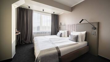 A modern hotel room with a large bed, a bedside table, a lamp, and a window with curtains.