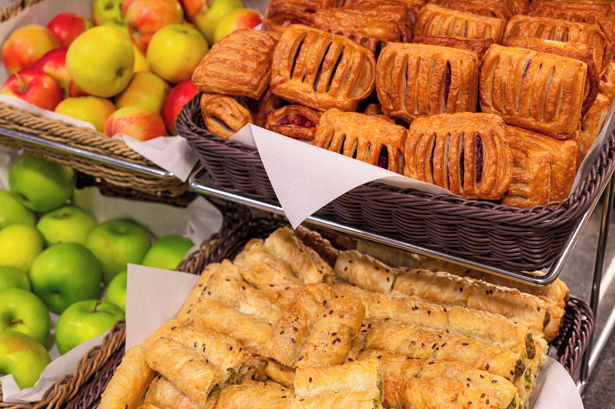 A display of pastries and apples in baskets.