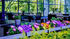 An outdoor seating area with tables and chairs, surrounded by large windows and potted plants. - Bellevue Park Hotel Riga (Riga)