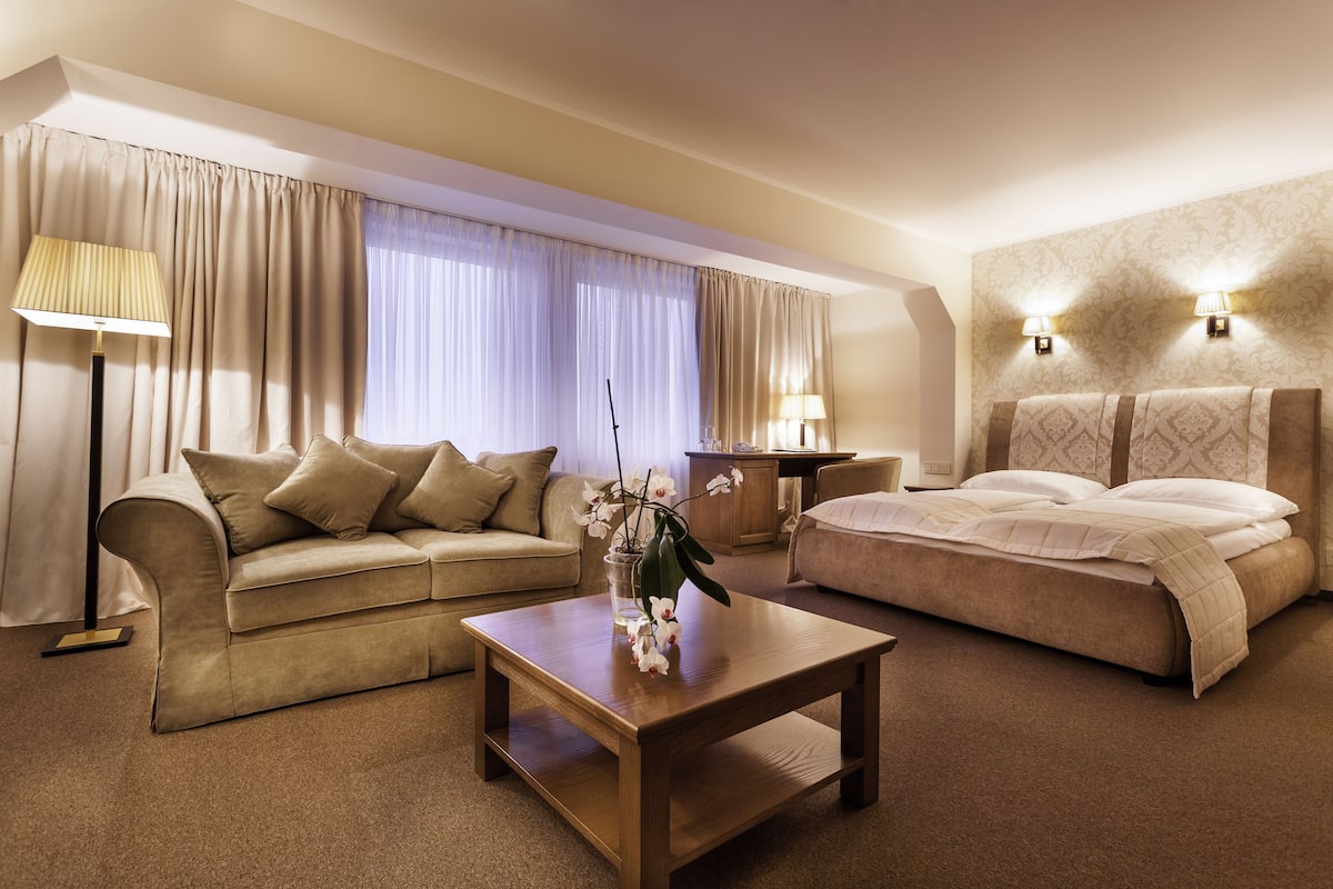 A hotel room with a bed, a sofa, a coffee table, and two lamps.