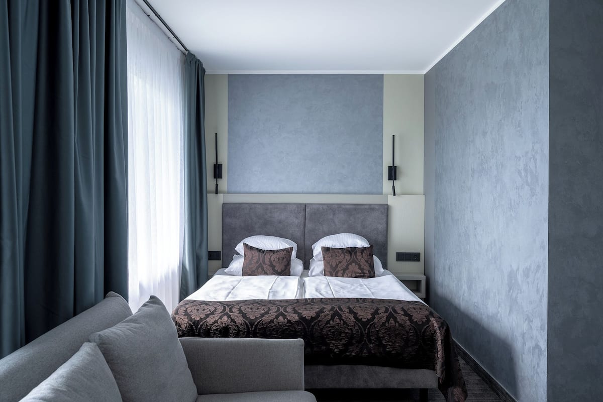A modern hotel room with a large bed, a sofa, and a view of the city.