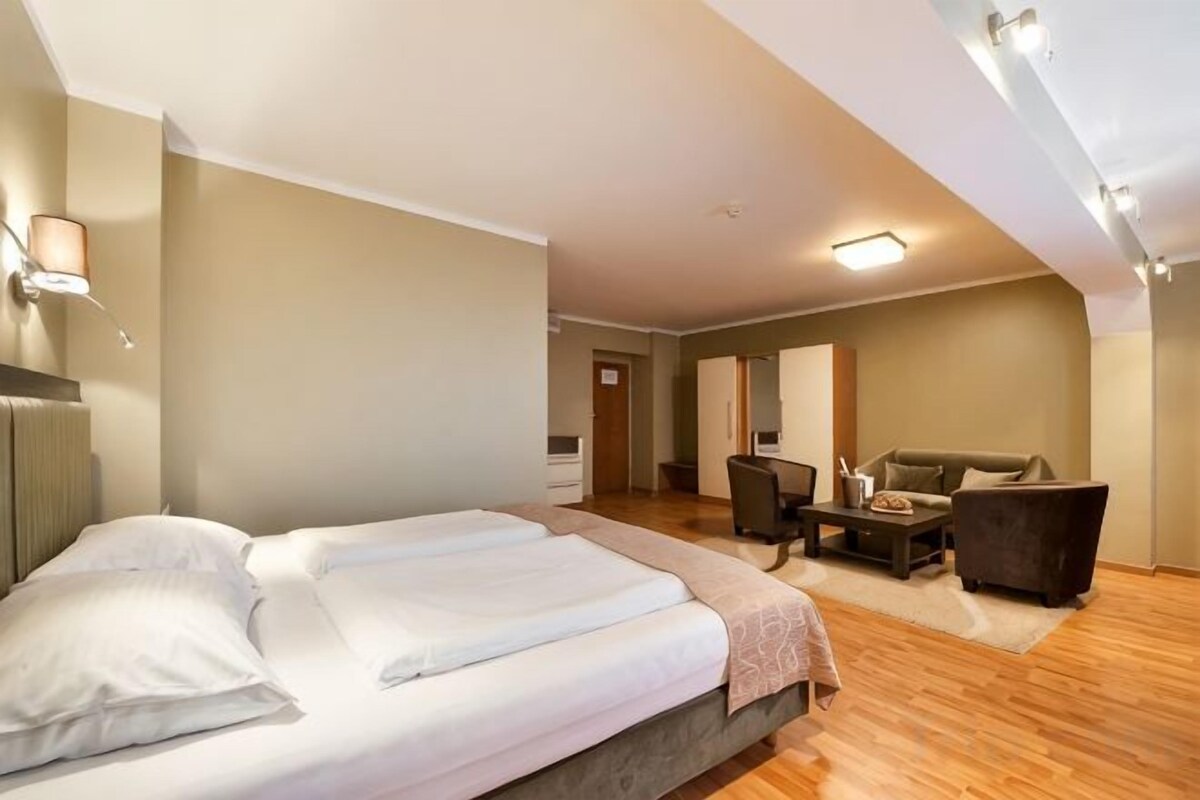 A hotel room with a bed, a desk, a chair, and a sofa.