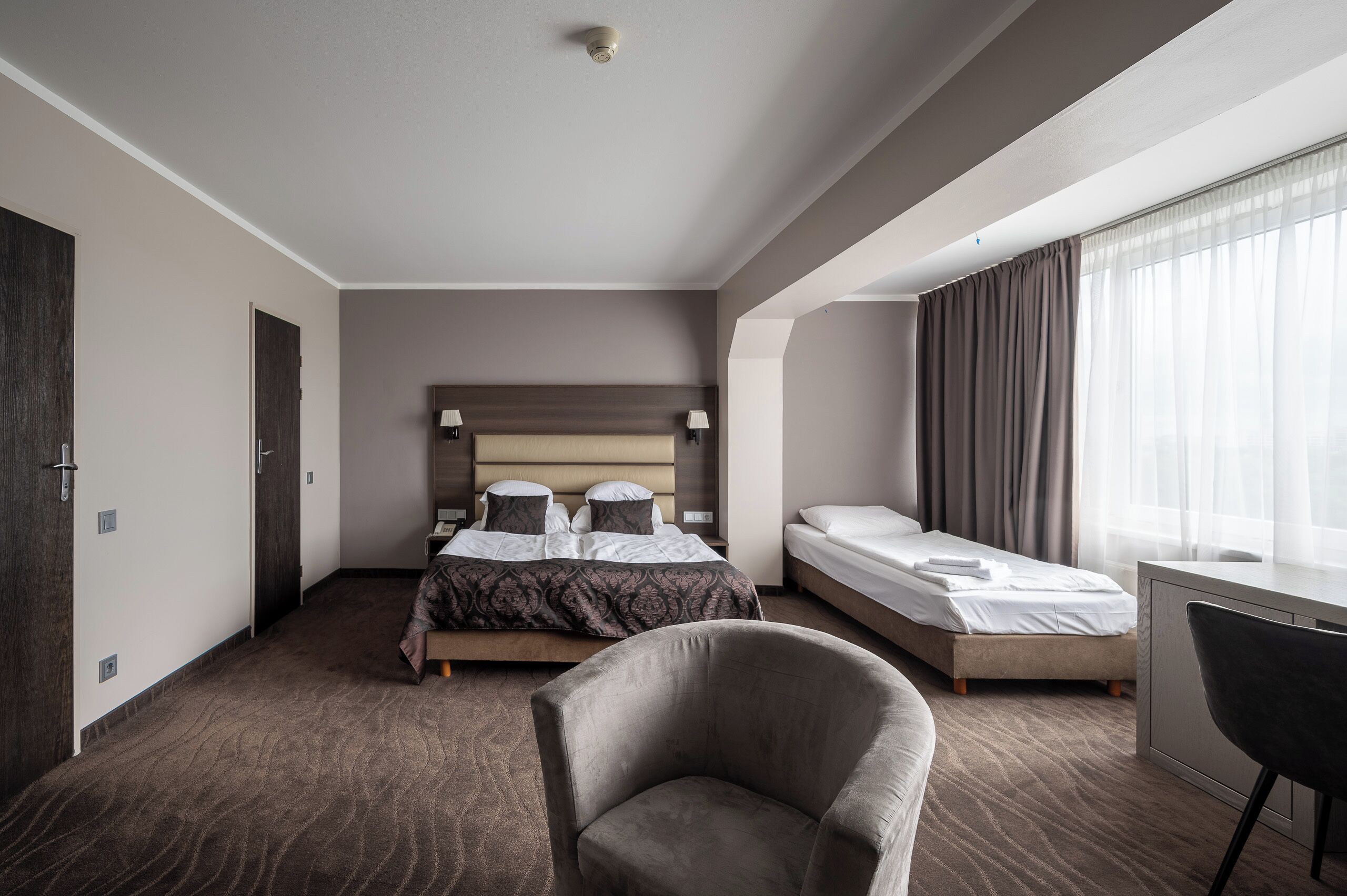 Quarto de hotel com uma cama grande, uma cama menor, uma escrivaninha e uma cadeira.