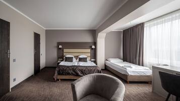 Quarto de hotel com uma cama grande, uma cama menor, uma escrivaninha e uma cadeira.