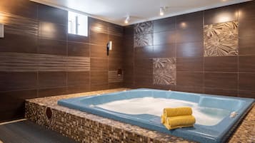 Relax in a spacious bathroom featuring a large hot tub with heater and control panel, surrounded by dark tile walls with subtle patterns.
