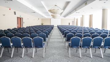 Un salón de conferencias con filas de sillas azules, piso alfombrado y techo blanco con ventilación.