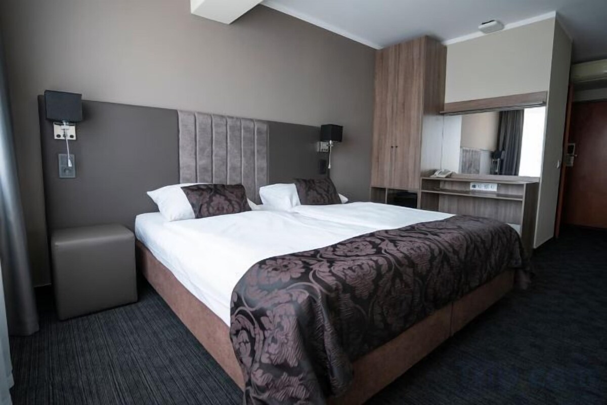 A hotel room with a large bed, bedside tables, a desk, and a mirror.